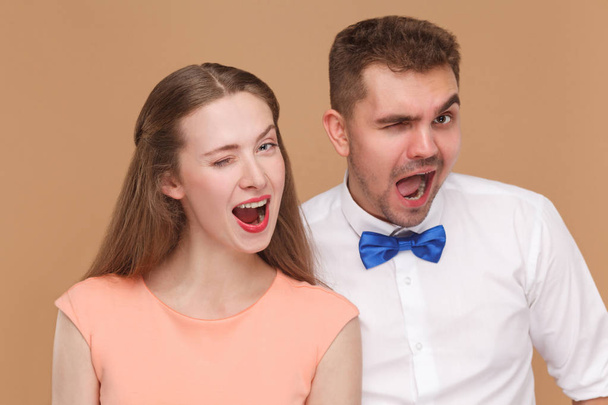 portrait of handsome man and beautiful woman looking at camera with funny faces and opened mouths and winking on brown background. - Photo, Image