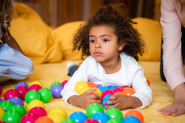 adorable african american kid lying on carpet with toys in kindergarten and looking away - Photo, image