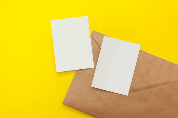 two blank postcards with large brown envelope on a yellow background. Copyspace, flatlay, mockup for design - Фото, изображение