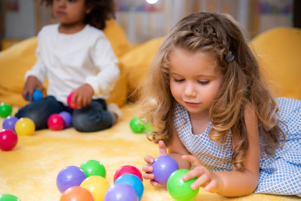 multicultural kids playing with colorful balls on carpet in kindergarten - Foto, Imagen