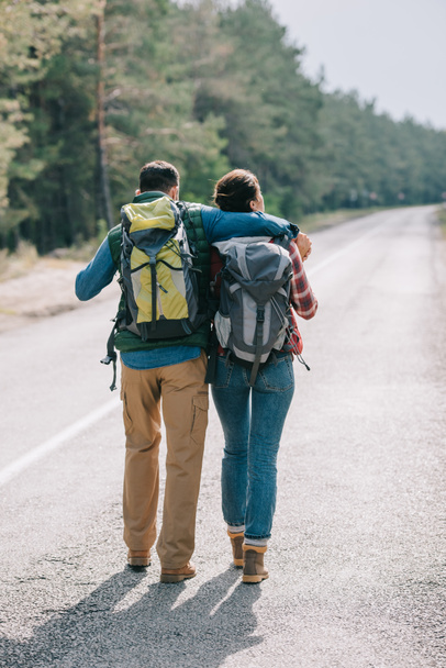 back view of couple of travelers with backpacks walking on road - Foto, imagen