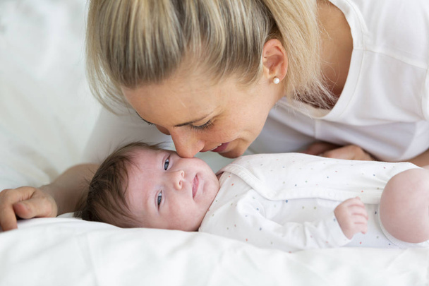 beautiful blond woman with white shirt is cuddling with her baby daughter in bed - Valokuva, kuva