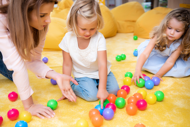 educator gesturing on colored balls to kids in kindergarten, child pointing on one - Foto, afbeelding