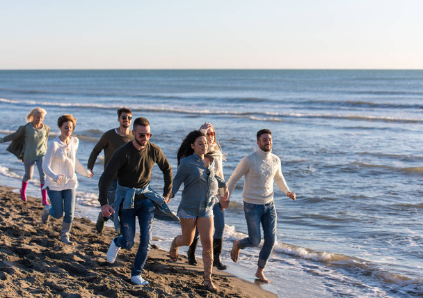 group of young friends spending day together running on the beach during autumn day - Фото, зображення