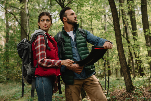 man and woman looking for destination on map while hiking in forest together - Photo, Image