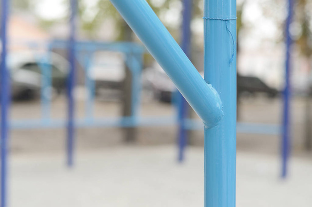Blue metal pipes and cross-bars against a street sports field for training in athletics. Outdoor athletic gym equipment. Macro photo with selective focus and extremely blurred background - Photo, Image