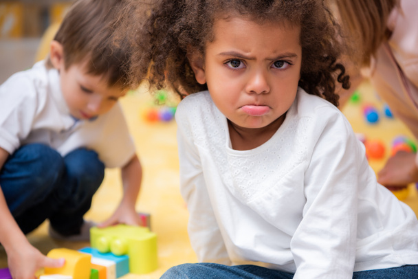 criança afro-americana insatisfeita sorrindo e olhando para a câmera no jardim de infância
 - Foto, Imagem