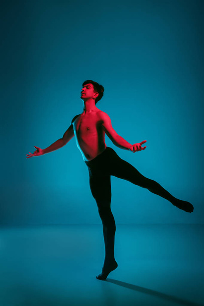 The male athletic ballet dancer performing dance on blue background. Studio shot. Ballet concept. Fit young man. Caucasian model - Fotografie, Obrázek