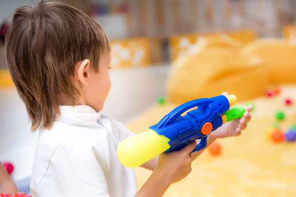 visão lateral do menino brincando com arma de água no jardim de infância
 - Foto, Imagem