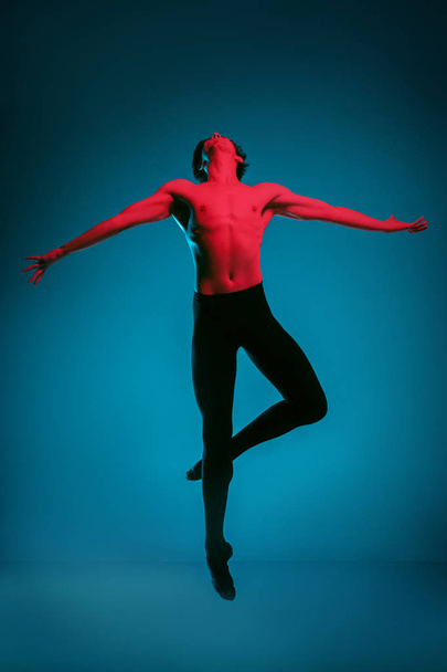 The male athletic ballet dancer performing dance on blue background. Studio shot. Ballet concept. Fit young man. Caucasian model - Photo, image