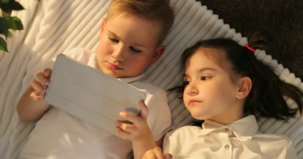 Top view of brother and sister using tablet while lying in floor. Portrait of little kids looking at touch pad at home - Filmagem, Vídeo