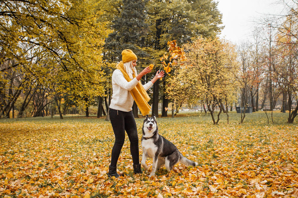 Mujer alegre y perro husky jugando juntos al aire libre en el parque de otoño
  - Foto, imagen