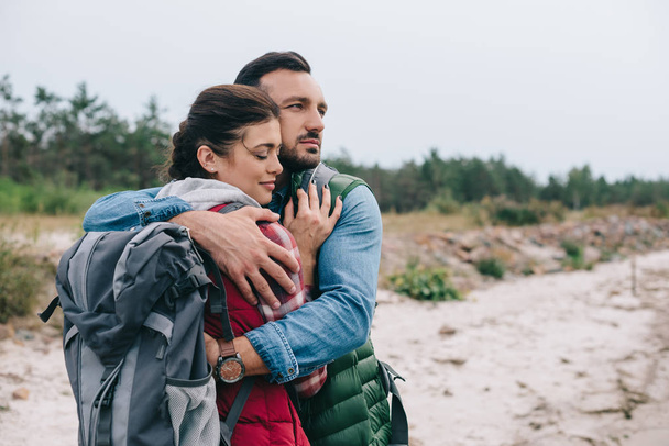 couple of hikers with backpacks hugging on sandy beach - Photo, Image