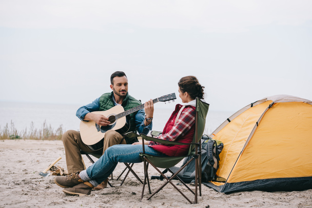 hombre tocando la guitarra acústica para la esposa en camping
 - Foto, Imagen