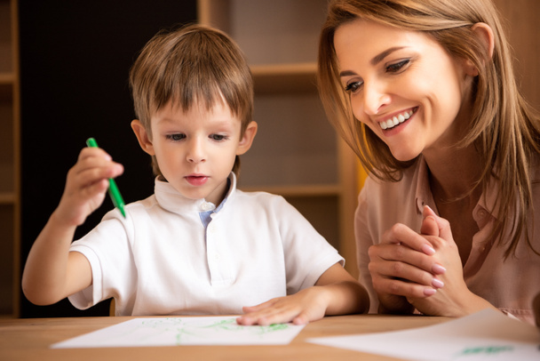 educador sonriente mirando al niño dibujando en el jardín de infantes
 - Foto, imagen