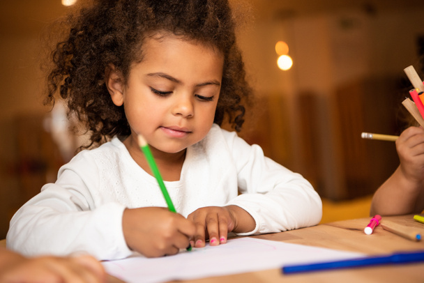 adorable african american kid erasing pencil from sheet of paper in kindergarten - Photo, Image