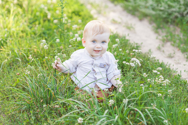 Portrait of cute little blonde boy sitting on the grass - Foto, afbeelding