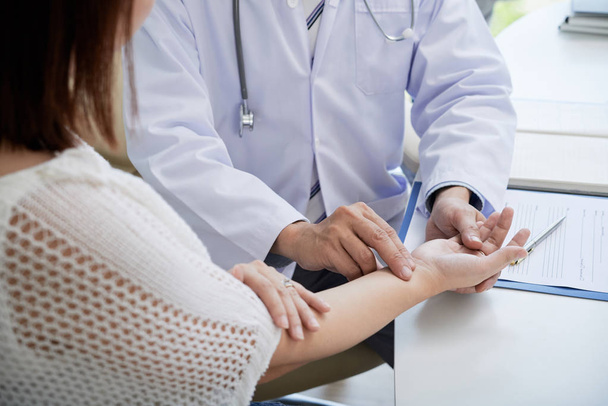 Arzt berührt Handgelenk einer Patientin, um Puls zu kontrollieren - Foto, Bild