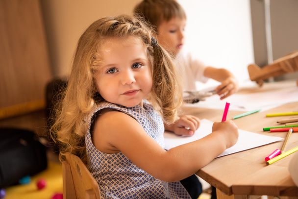 adorable kid drawing in kindergarten and looking at camera - Photo, Image