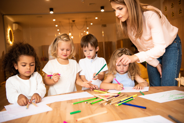 Pädagogin sieht multiethnische Kinder im Kindergarten zeichnen - Foto, Bild