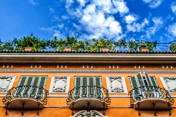 Balcones forjados en un hermoso edificio naranja con balcones verdes sobre un fondo de cielo azul con nubes azules esponjosas
. - Foto, Imagen