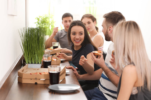 Jóvenes comiendo pizza en la mesa adentro
 - Foto, imagen