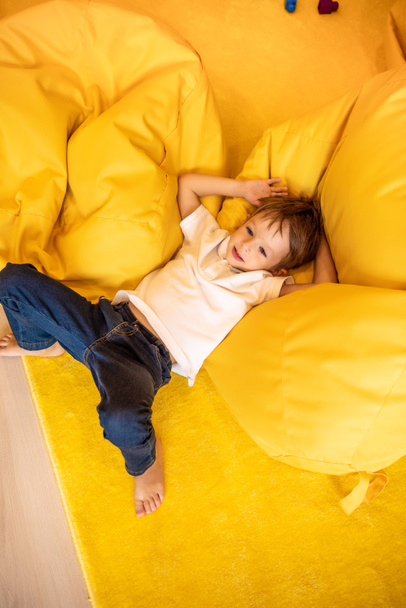 high angle view of adorable boy lying on bean bag chair in kindergarten - Photo, Image