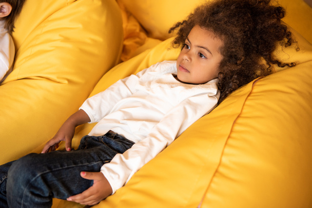 high angle view of adorable african american kid lying on bean bag chair in kindergarten - Foto, immagini