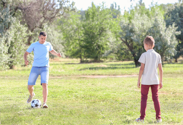 Μικρό αγόρι με τον μπαμπά του παίζοντας ποδόσφαιρο σε εξωτερικούς χώρους - Φωτογραφία, εικόνα