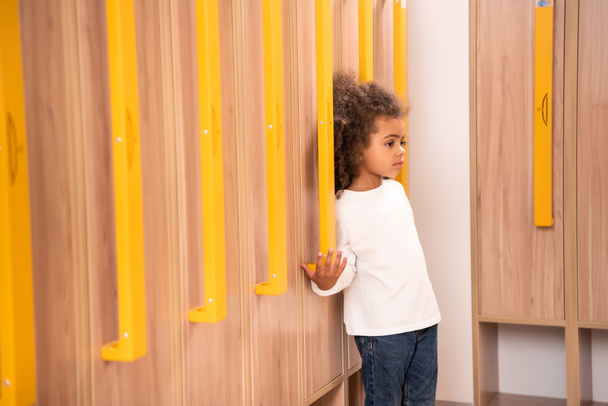 чарівна афроамериканська дитина стоїть біля дерев'яних шафок в дитячій гардеробній
 - Фото, зображення