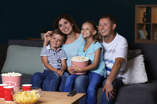 Familia feliz comiendo palomitas de maíz mientras ve la televisión por la noche
 - Foto, imagen