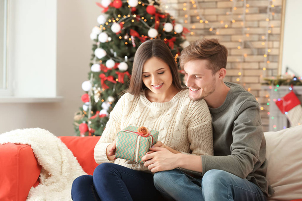 Χαριτωμένο νεαρό ζευγάρι με το δώρο Χριστουγέννων στο σπίτι - Φωτογραφία, εικόνα