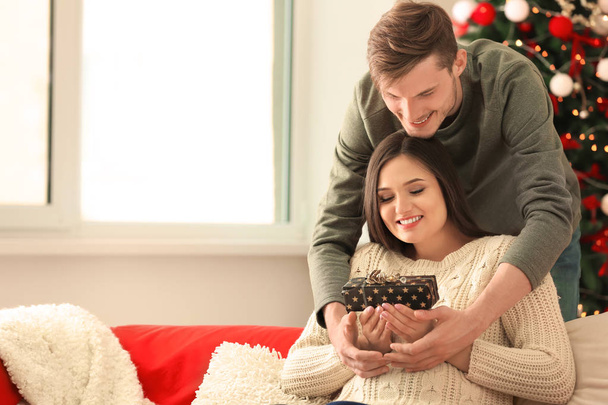 Young woman receiving Christmas gift from her husband at home - Foto, Imagen