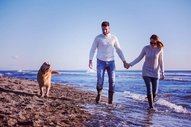 Couple Running On The Beach Holding Their Hands with dog On autmun day - Foto, afbeelding