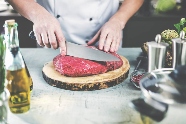 Chef in restaurant kitchen cooking,he is cutting meat or steak  - Foto, imagen