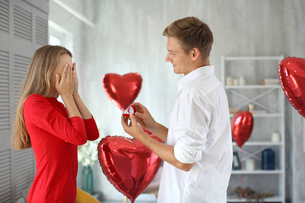 Young man proposing to his beloved with beautiful engagement ring at home - Foto, Imagen