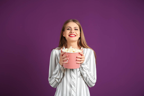 Beautiful young woman with cup of popcorn on color background - Photo, image