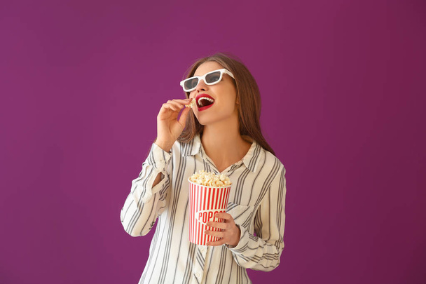 Beautiful young woman with cup of popcorn and 3D cinema glasses on color background - Fotó, kép