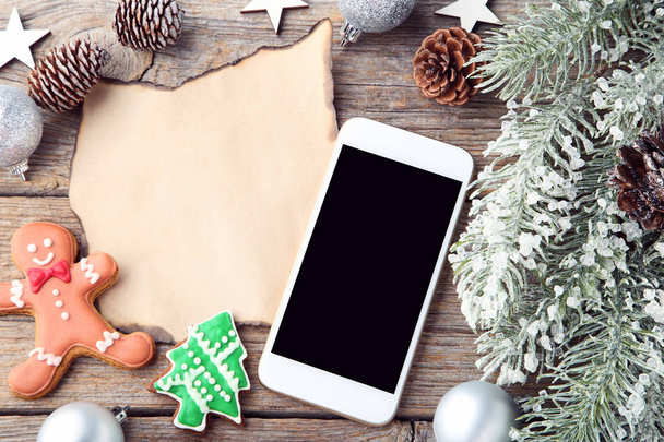 Smartphone with gingerbread cookies, fir-tree branches and sheet of blank paper on wooden background - Valokuva, kuva