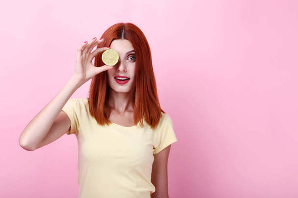 Young redhaired woman with lime on pink background - Foto, Bild