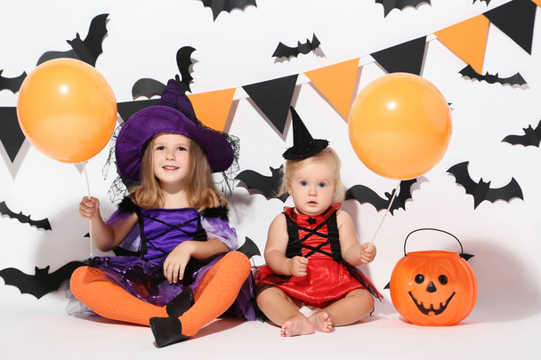 Little girls in halloween costumes with balloons sitting on white background - Photo, image