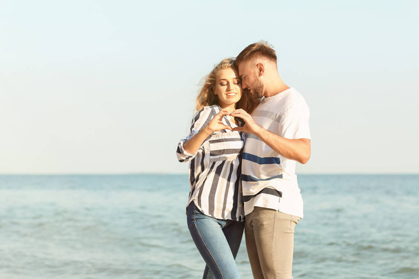 Cute young couple making heart with their hands on sea shore - Fotoğraf, Görsel