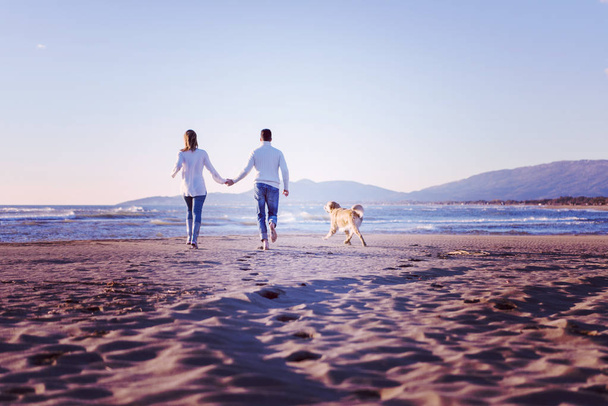 Couple Running On The Beach Holding Their Hands with dog On autmun day - Foto, afbeelding