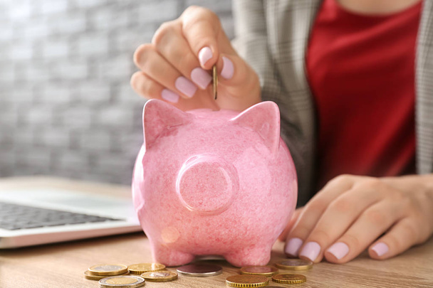 Mulher colocando moeda no banco porquinho na mesa
 - Foto, Imagem