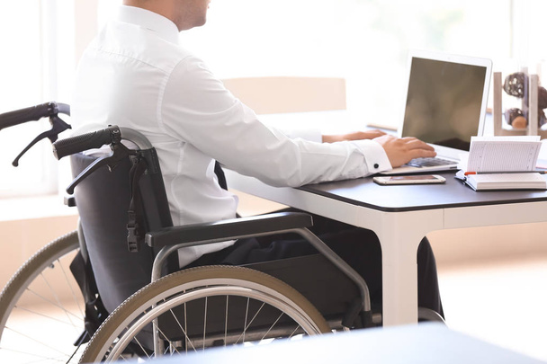 Бізнесмен в інвалідному візку, що працює з ноутбуком в офісі
 - Фото, зображення