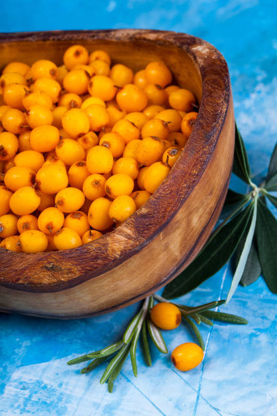 Sea buckthorn berries in wooden bowl on blue background - Photo, Image
