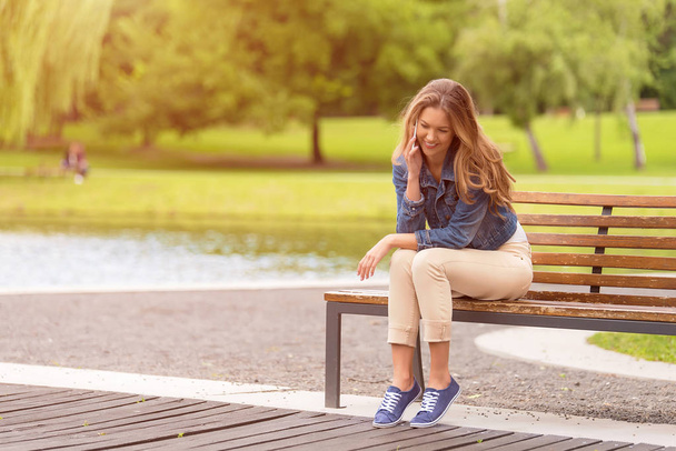 Young woman sitting on bench in the park - Fotoğraf, Görsel