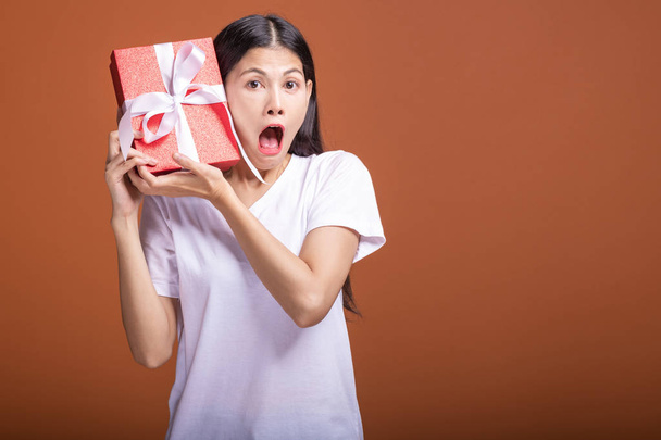Jonge hipster meisje kreeg een cadeau. Aziatische vrouw in wit t-shirt houden een rode aanwezig doos van de gift, schok uiterst stemming. De concept van de gift van de vakantie. verrassing stemming. Concept van vakantie cadeau. - Foto, afbeelding