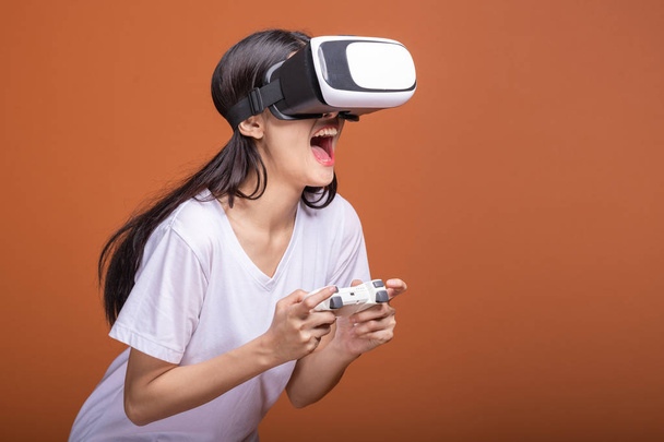 Woman wearing VR headset. Young Asian woman in white t-shirt with VR head gear, very excited pose. New entertainment concept. - Φωτογραφία, εικόνα
