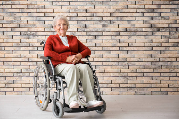 Senior mulher em cadeira de rodas contra parede de tijolo
 - Foto, Imagem